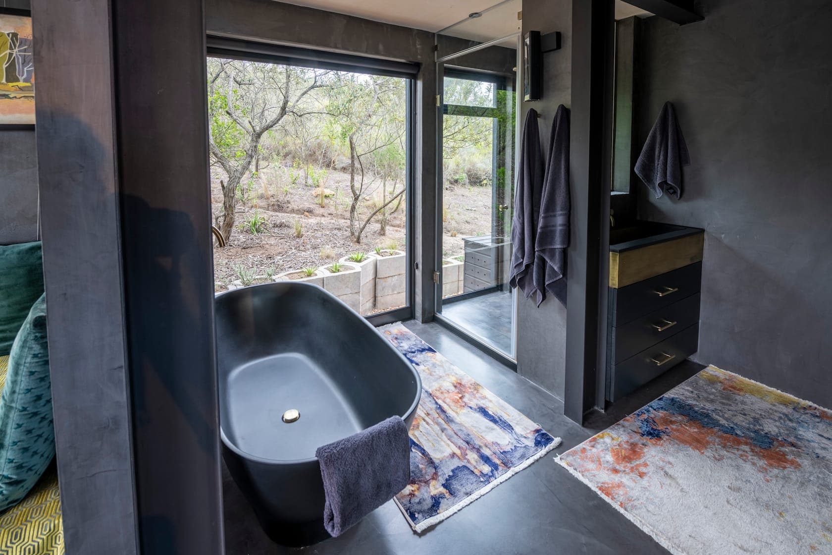 Black freestanding tub by a full-height window with a dark vanity