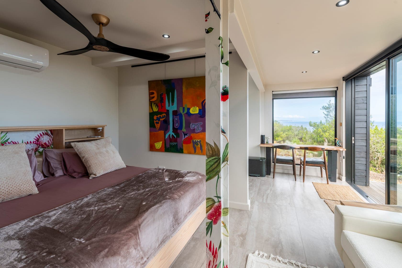Bright bedroom with bold artwork opening to a study area and ocean view