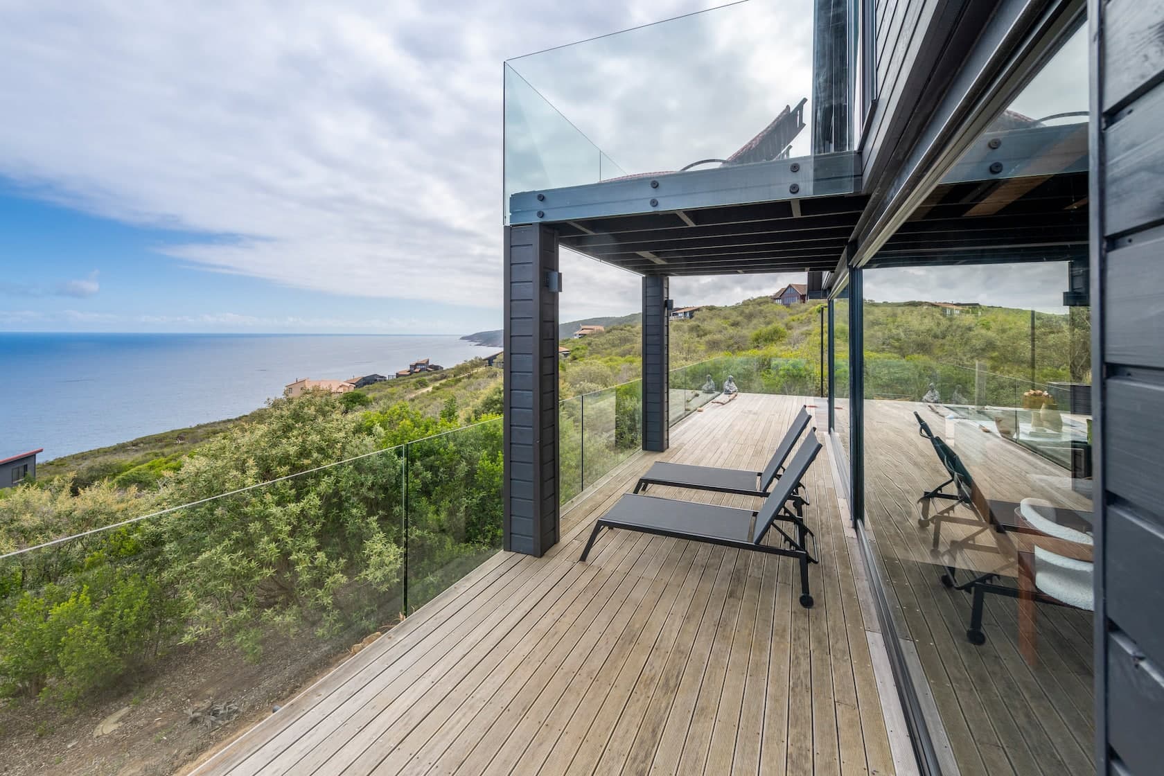Timber deck with sun loungers and a glass balustrade above the ocean