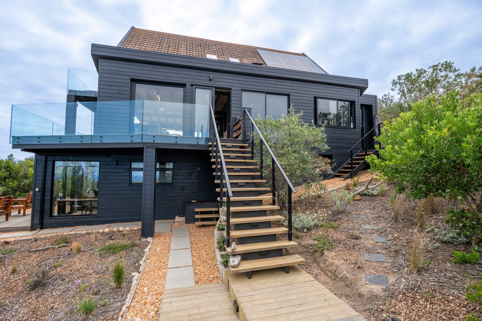 Black-clad two-storey home with timber stairs and a pathway to the entrance